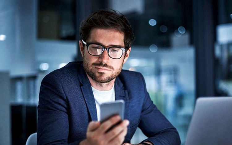 Geschäftsmann im Büro schaut auf sein Handy